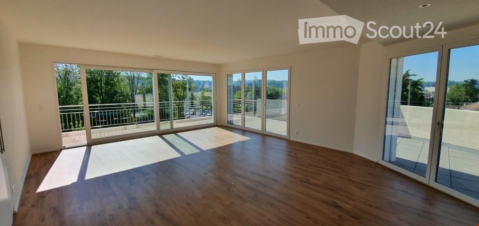 Spacious living room with large windows and sliding glass doors leading to a balcony or terrace, hardwood flooring, and an open layout.