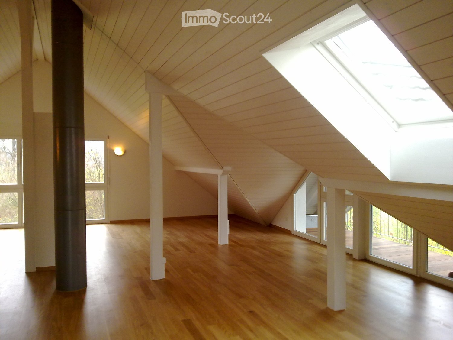 attic room, slanted ceiling, wooden floor, skylight, large windows, white walls, dark pillar, white columns, two glass doors leading to balcony