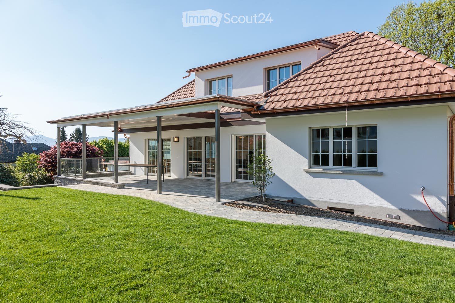modern white house, red tile roof, outdoor patio with table, large windows, lawn