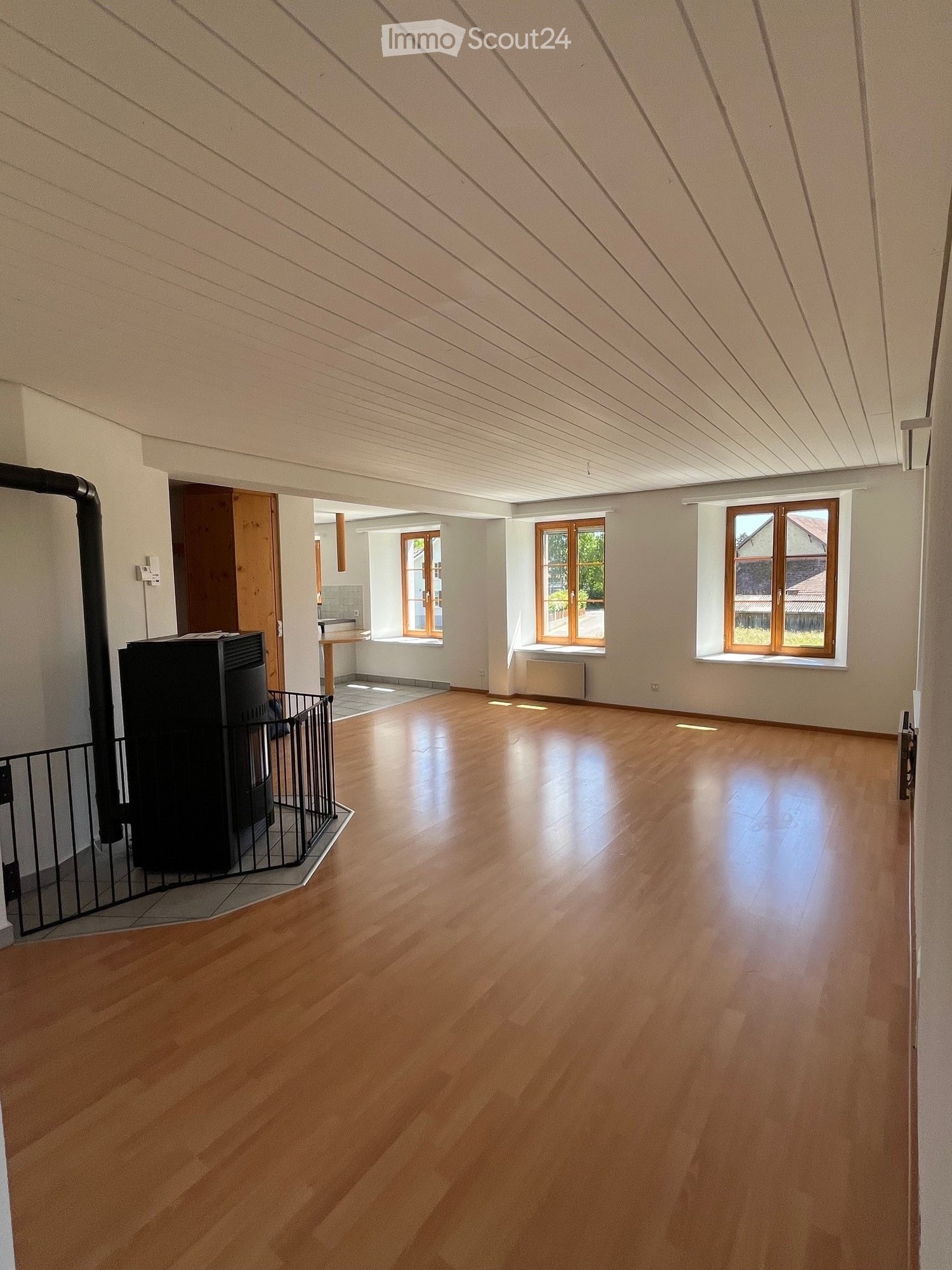 empty room with fireplace, white walls, wooden floor, 3 windows, radiators, wooden table, small black box, window sill, wooden cabinet