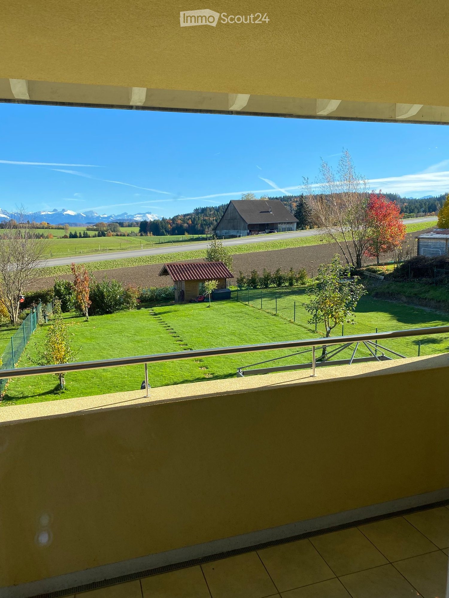 spacious balcony, metallic railing, large open lawn, small shed, trees, and mountains