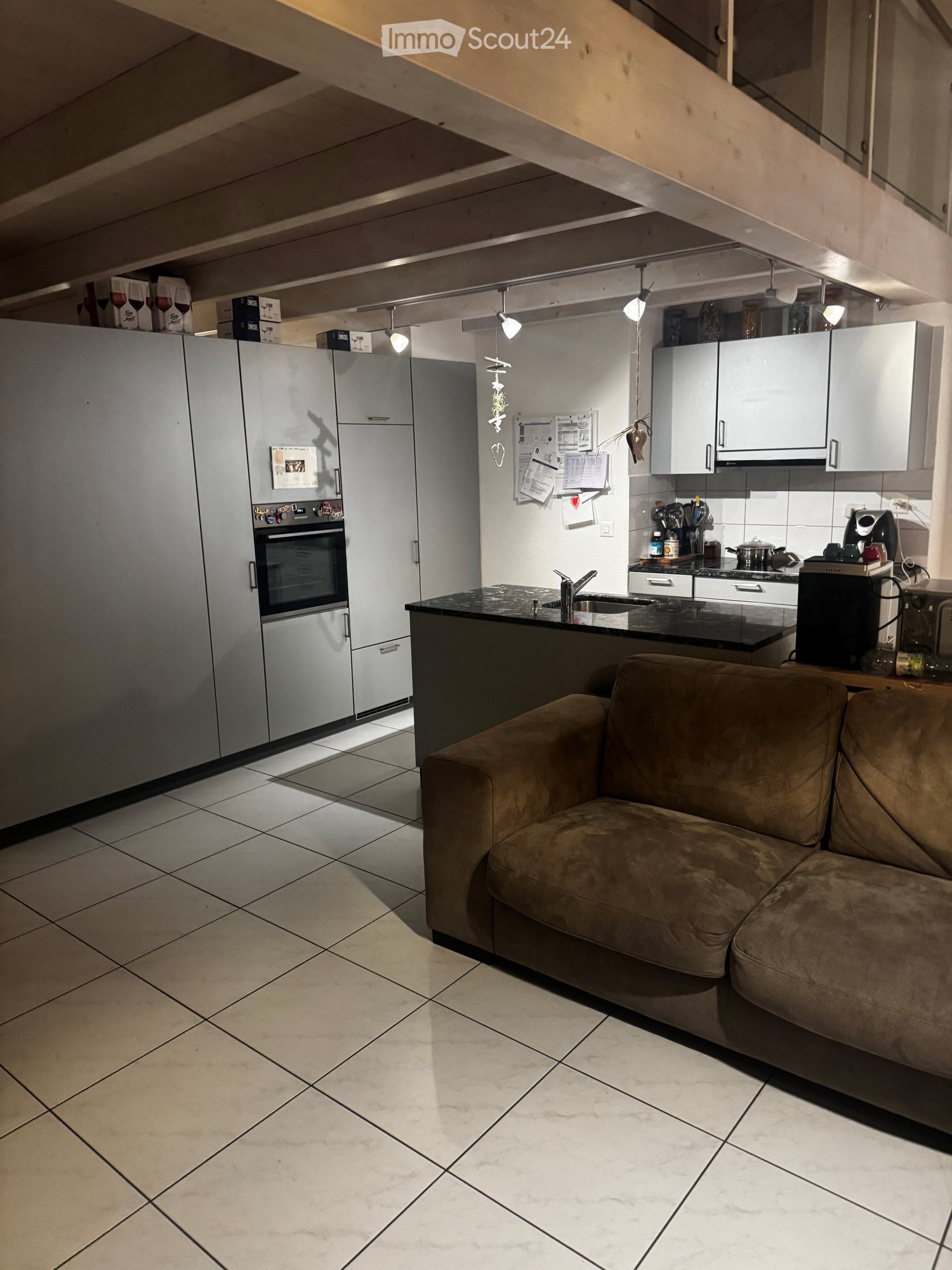 Open space kitchen and living area, raised ground floor, white tiled flooring, modern appliances, central island, large brown couch