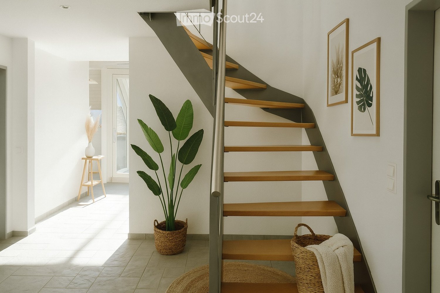 White tiled flooring, modern staircase with gray handrail, decorative plant in a basket, baskets with towels, framed pictures on the wall