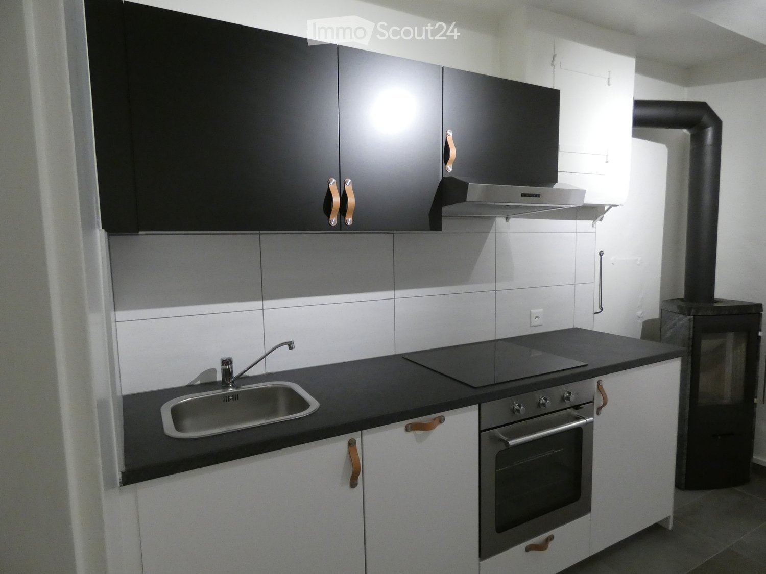 modern fitted kitchen, stainless steel sink, oven, induction cooktop, black countertops, white cabinets, black cabinets, exhaust fan, fireplace