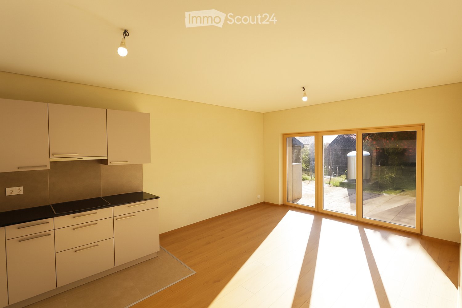 empty kitchen with cabinets, sliding glass doors leading to patio, windows, wooden floor, white walls, two lamps