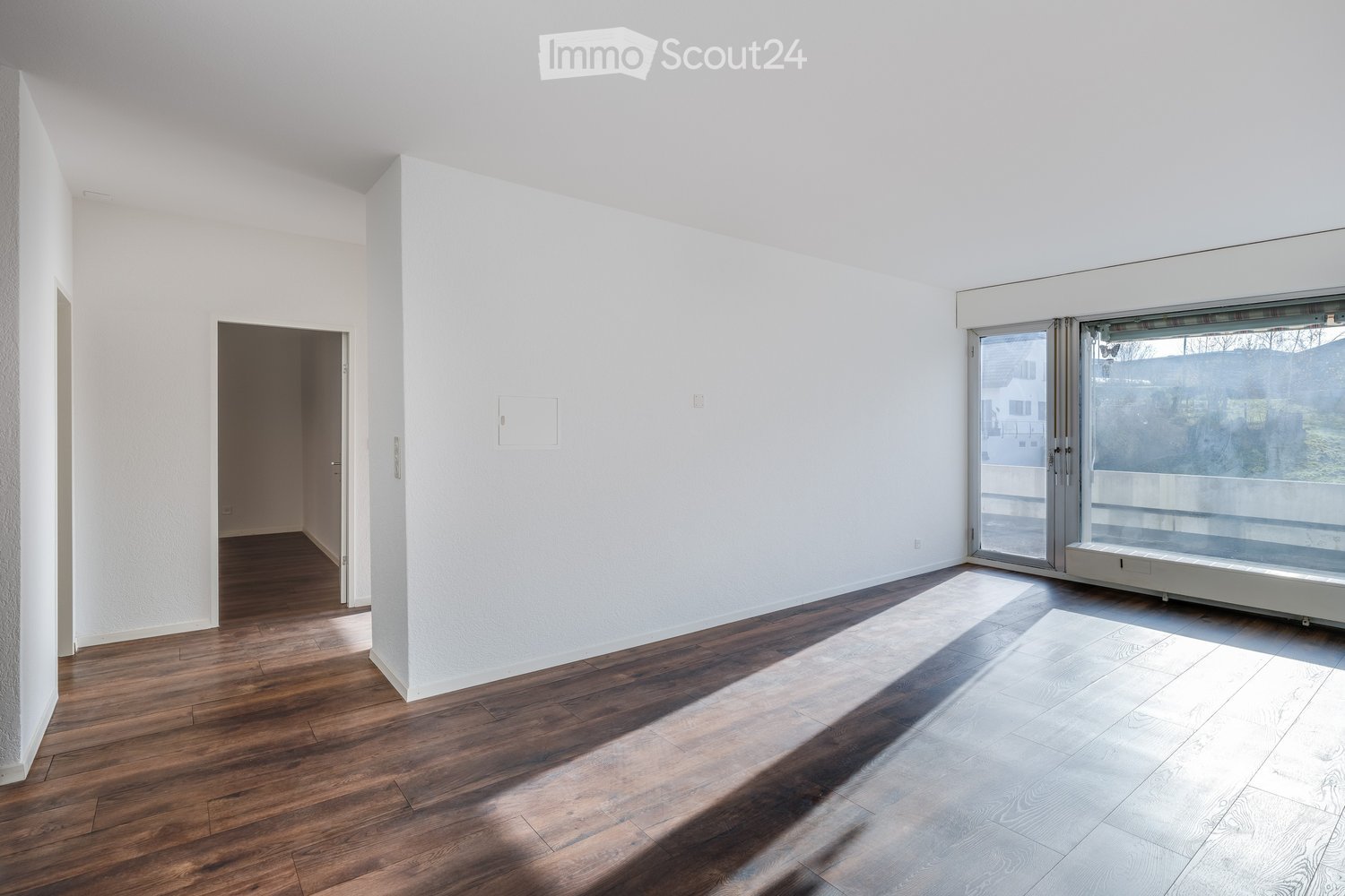 An empty room with white walls, wooden flooring, a glass sliding door, and a balcony