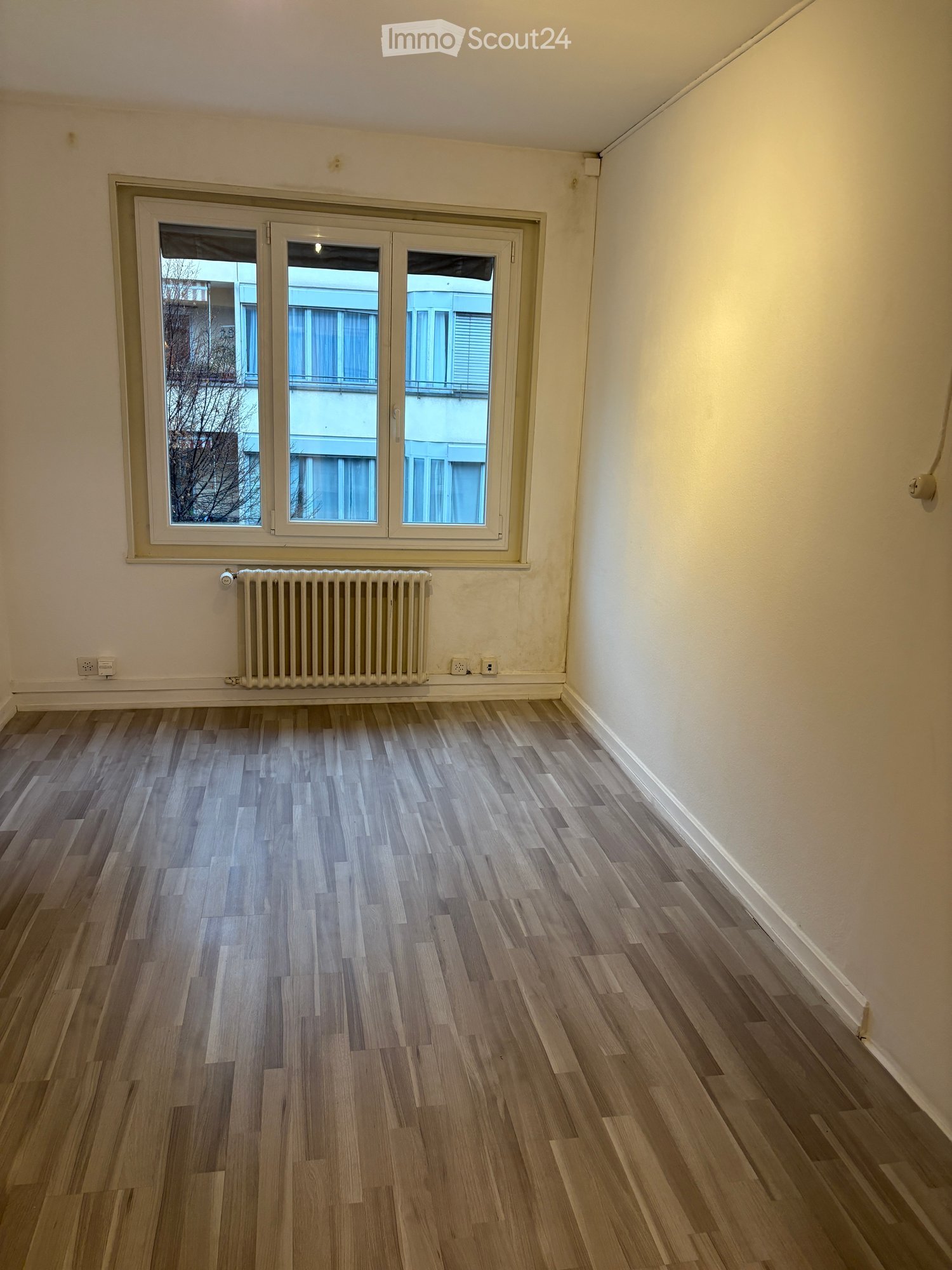 empty room with hardwood floors, white walls, large window, radiator