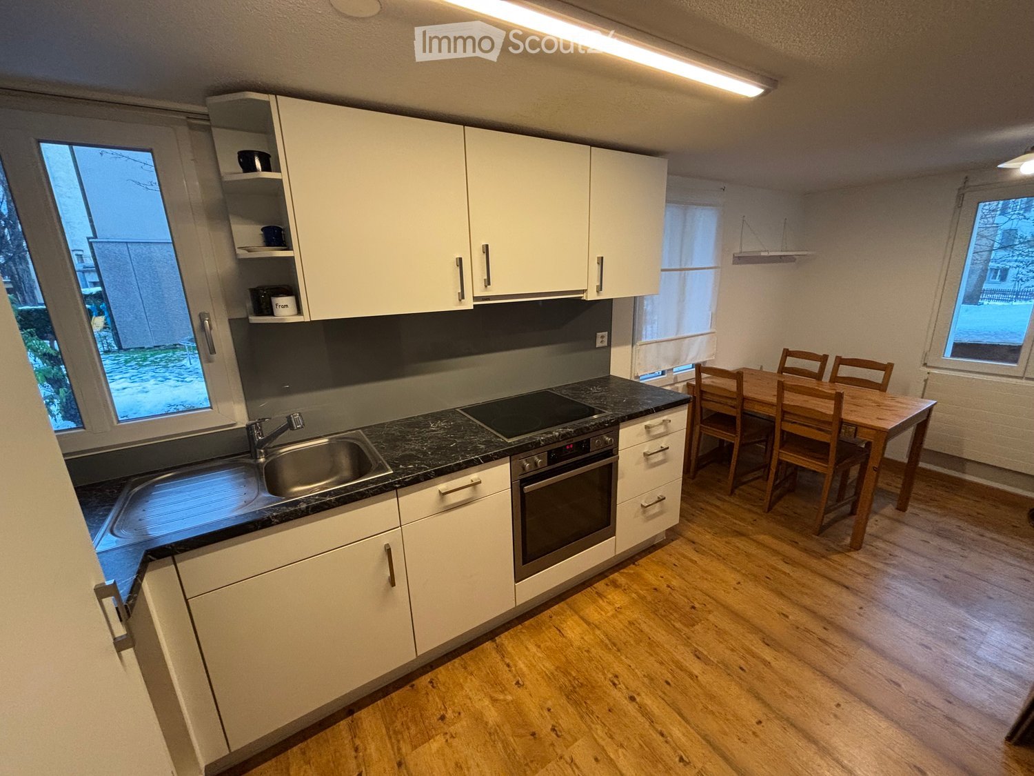 a modern, open-plan kitchen, with large window, modern appliances, and wooden dining table