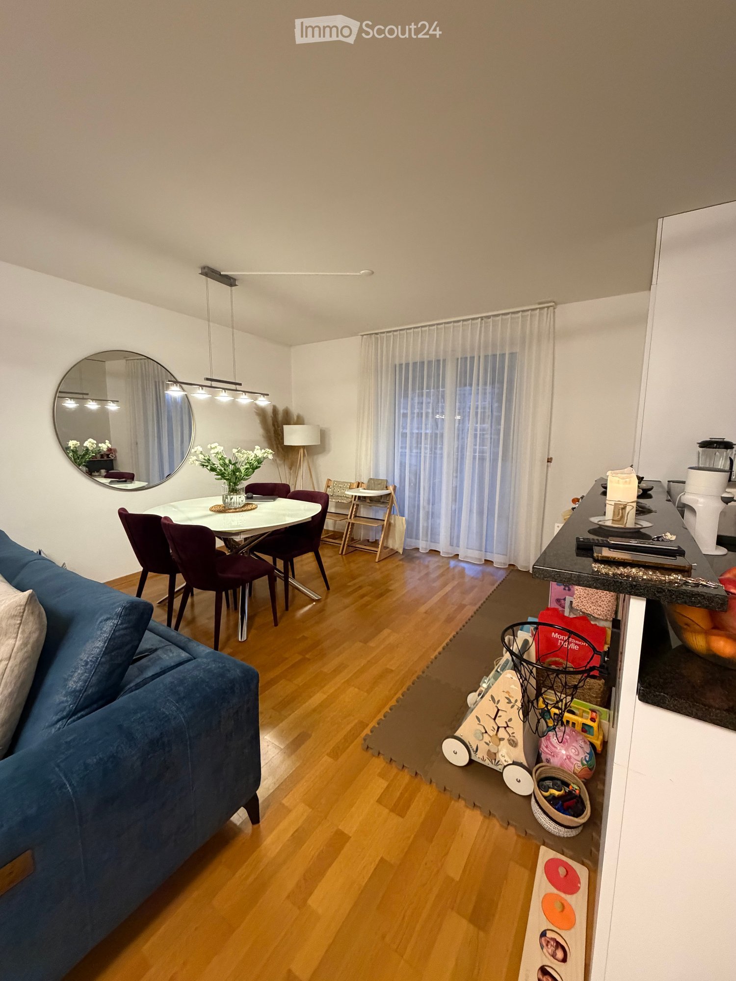 Open-plan living and dining area, wooden floors, blue sofa, white dining table and chairs, decorative items, large mirror