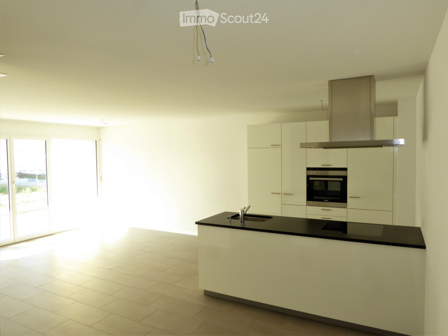 Modern kitchen with white cabinetry, black countertop, stainless steel appliances, and a glass door leading to an outdoor area.