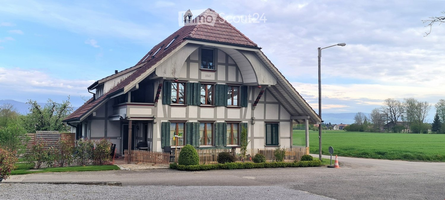 white and brown exterior, red roof, several windows, wooden fence, small gravel driveway