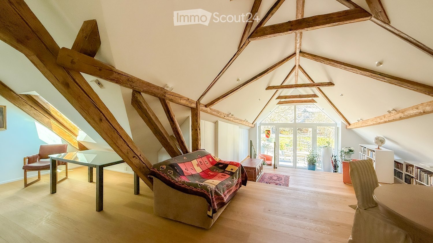 Attic room with wooden beams, wooden flooring, wooden table, covered couch, chairs, rug, shelf, potted plants, French windows