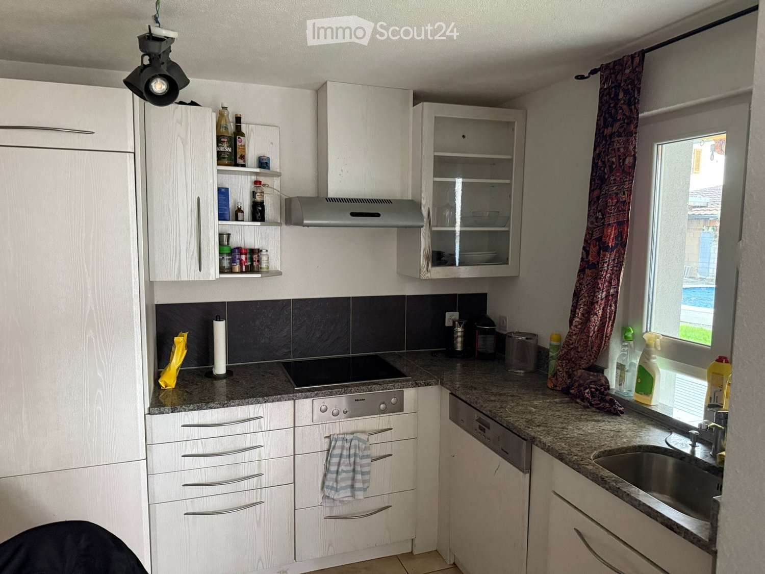 A fully furnished kitchen with an island, white cabinets, granite countertops, built-in oven, and dishwasher