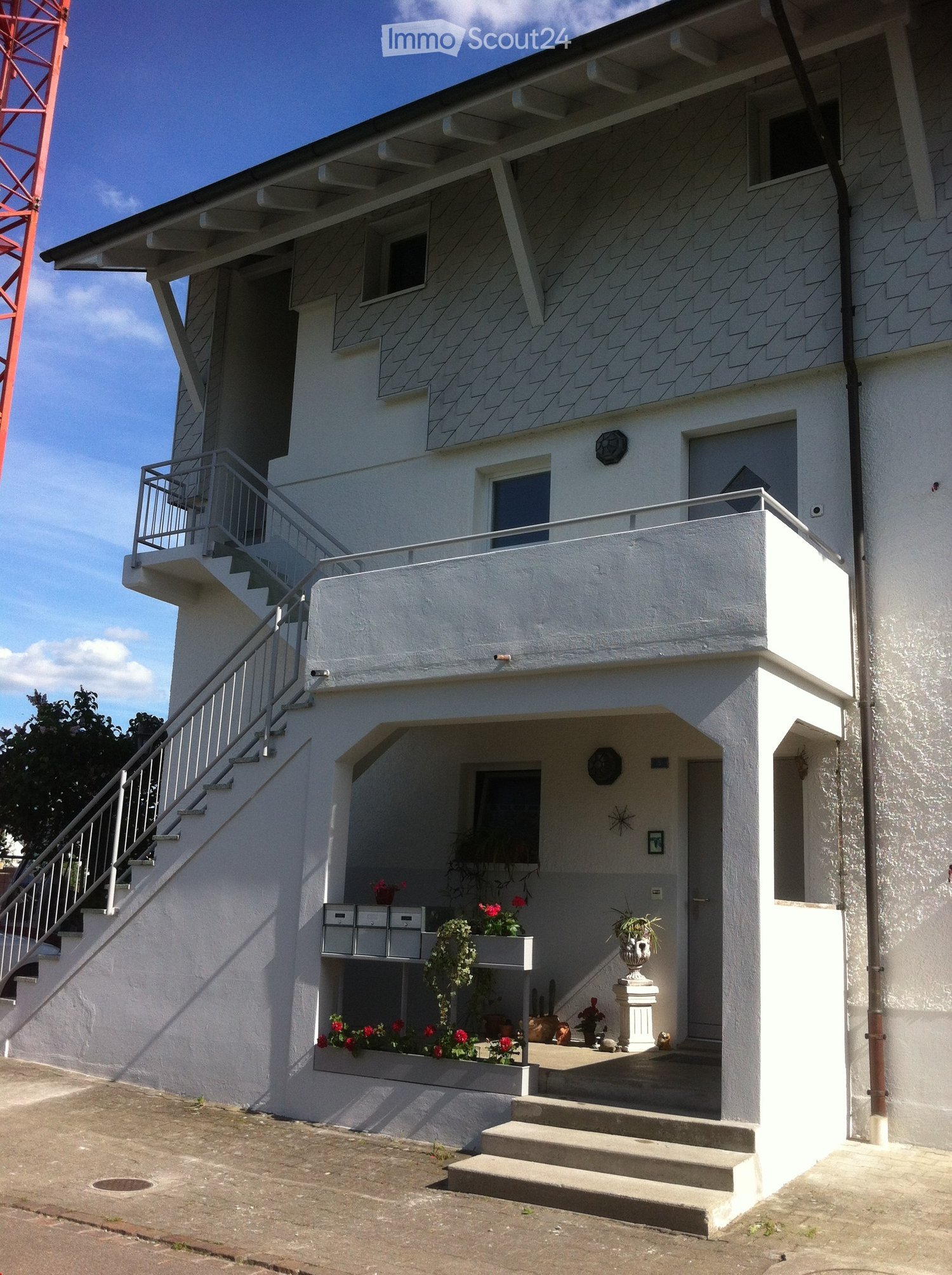 2 story white building, front balcony, metal staircase, flower boxes on first floor, mailbox on balcony