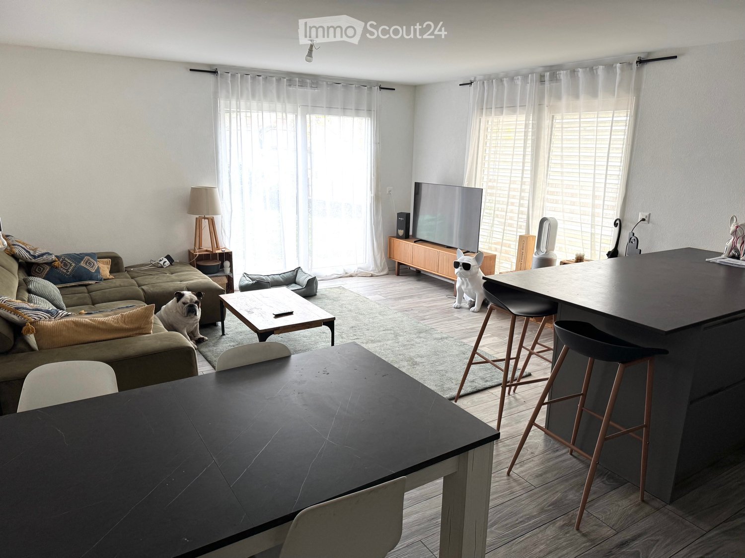 Modern living room with couch, coffee table, TV, carpet, and dining table with stools.