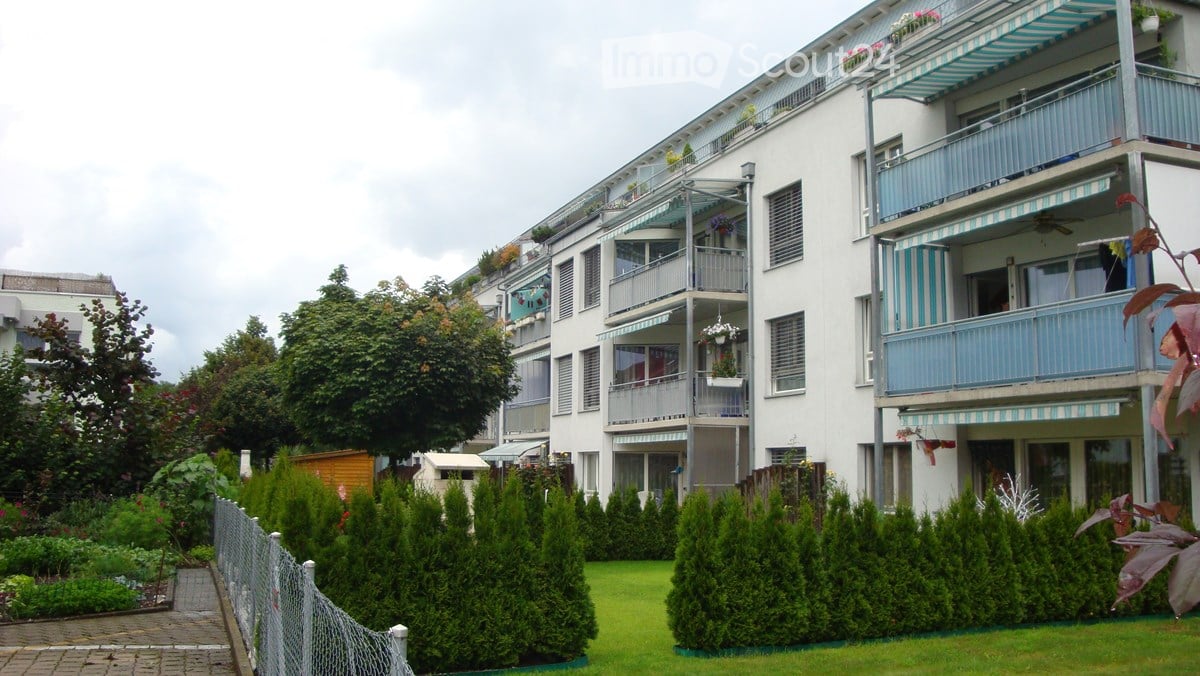 white, multi-story building, balconies, fenced garden, greenery