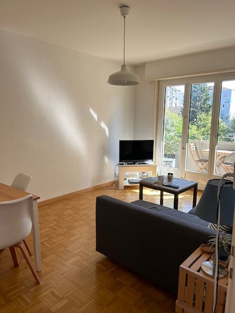 Living room with couch, coffee table, TV stand, dining table, white walls, wooden floor, glass doors to balcony