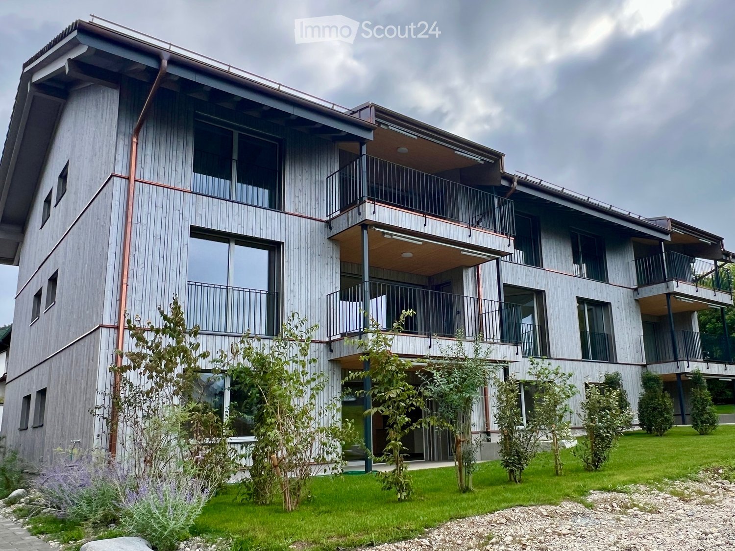multi story building, wood facade, many windows, copper pipes, balconies, green lawn