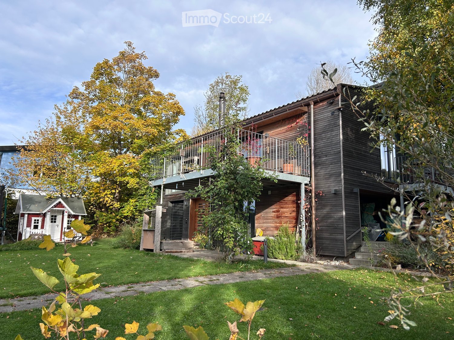 Contemporary house, wood exterior, green lawn, large trees, small balcony on second floor