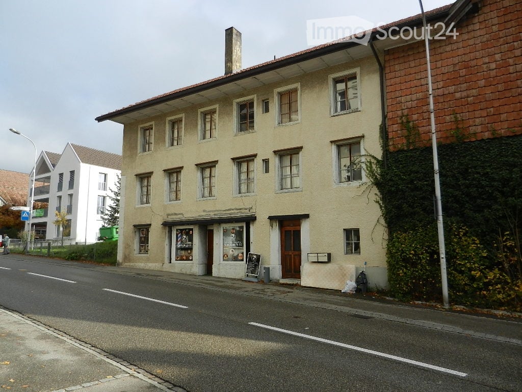 Two-story building with multiple windows, brick chimney, a shop at the ground floor, a street light and grass in front