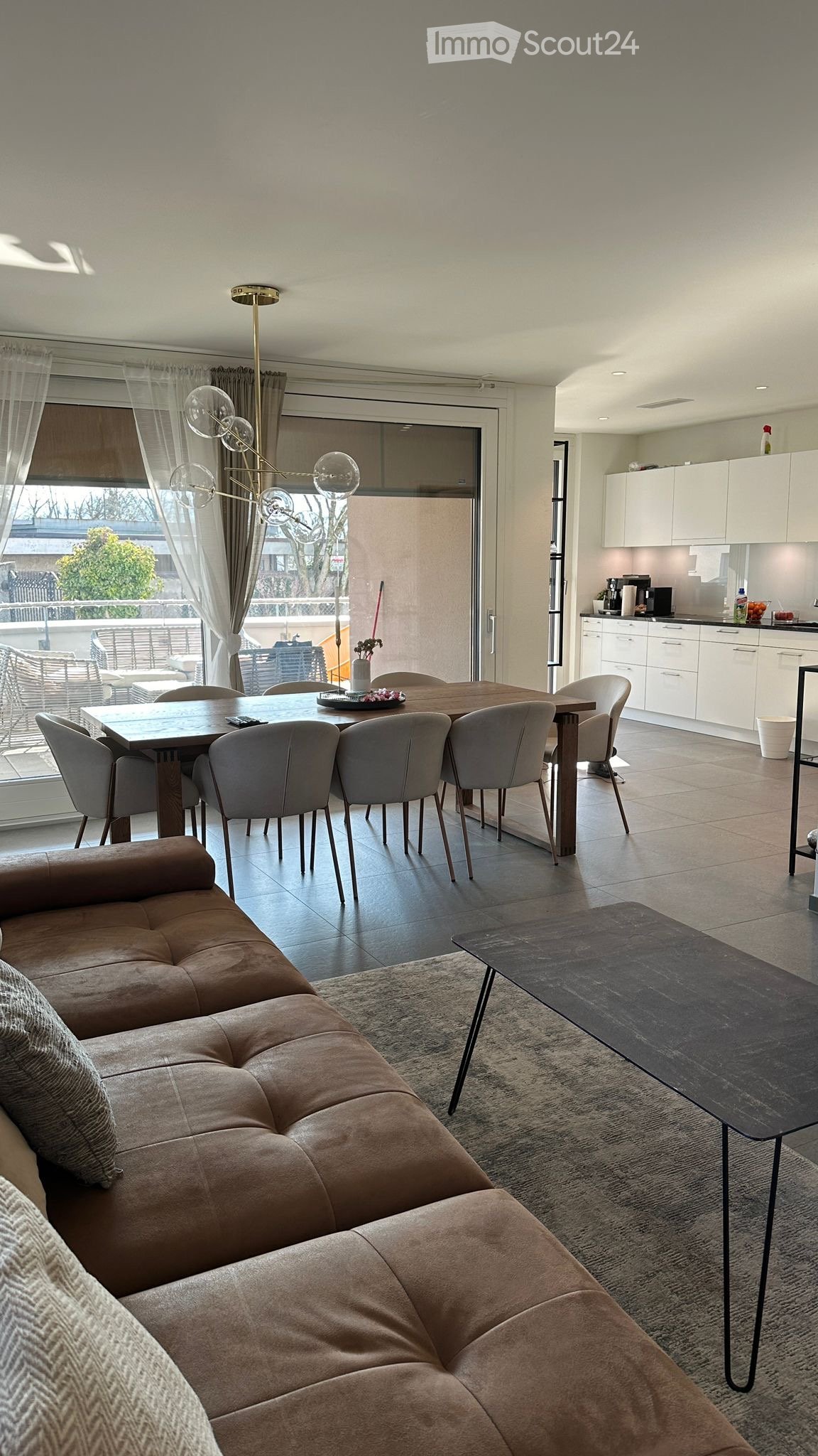 brown couch, wooden table, large windows, balcony, large floor lamp, coffee table