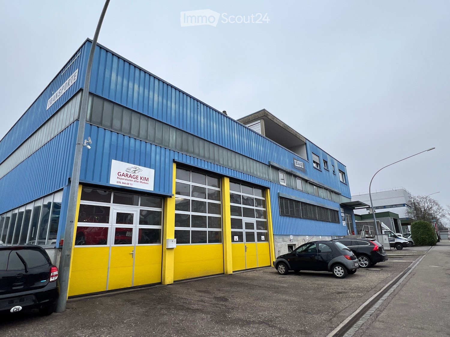 Blue industrial building with large yellow garage doors and multiple windows. Garage Kim written on front.