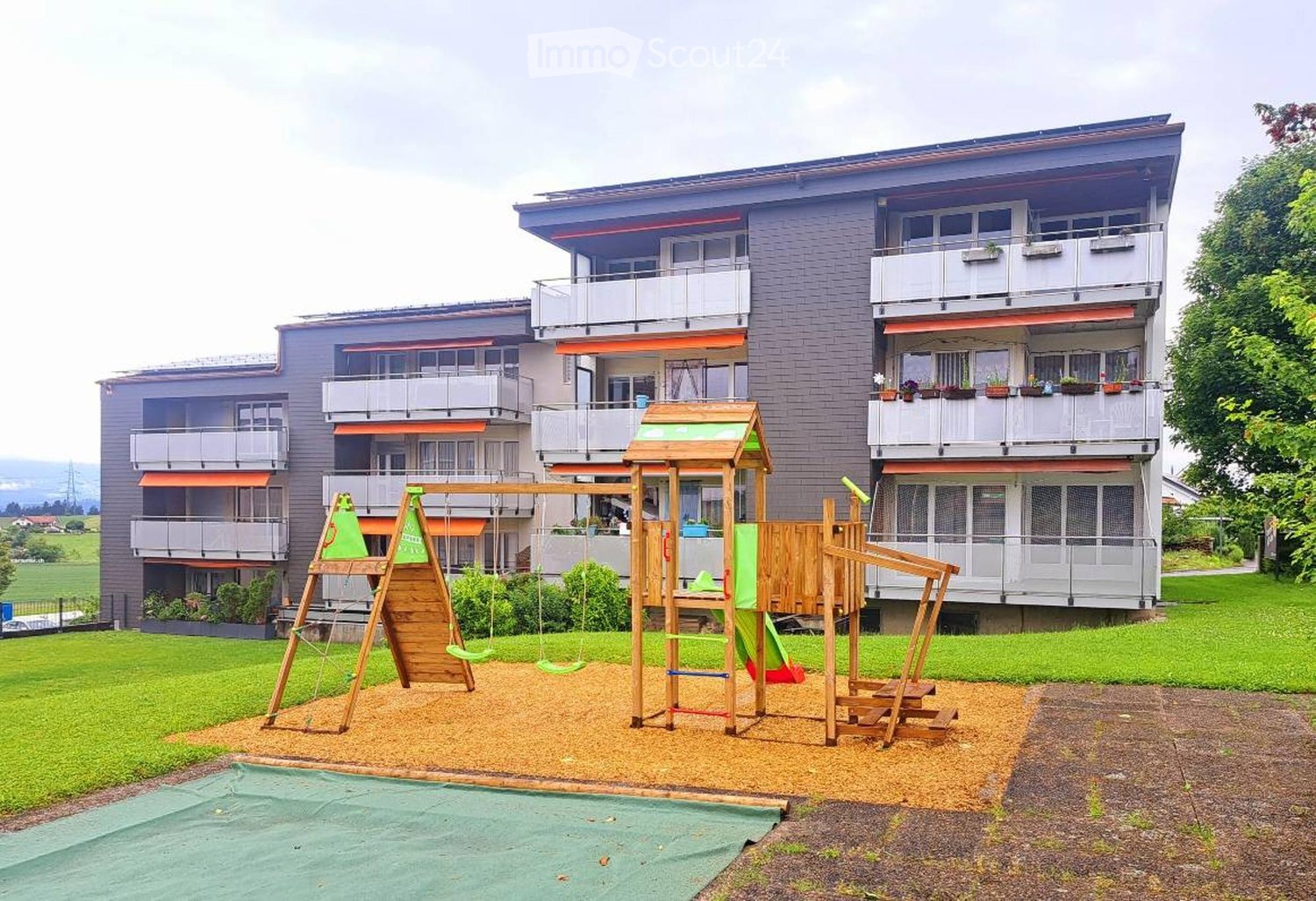 3 story apartment building, multiple balconies, green lawn, playground