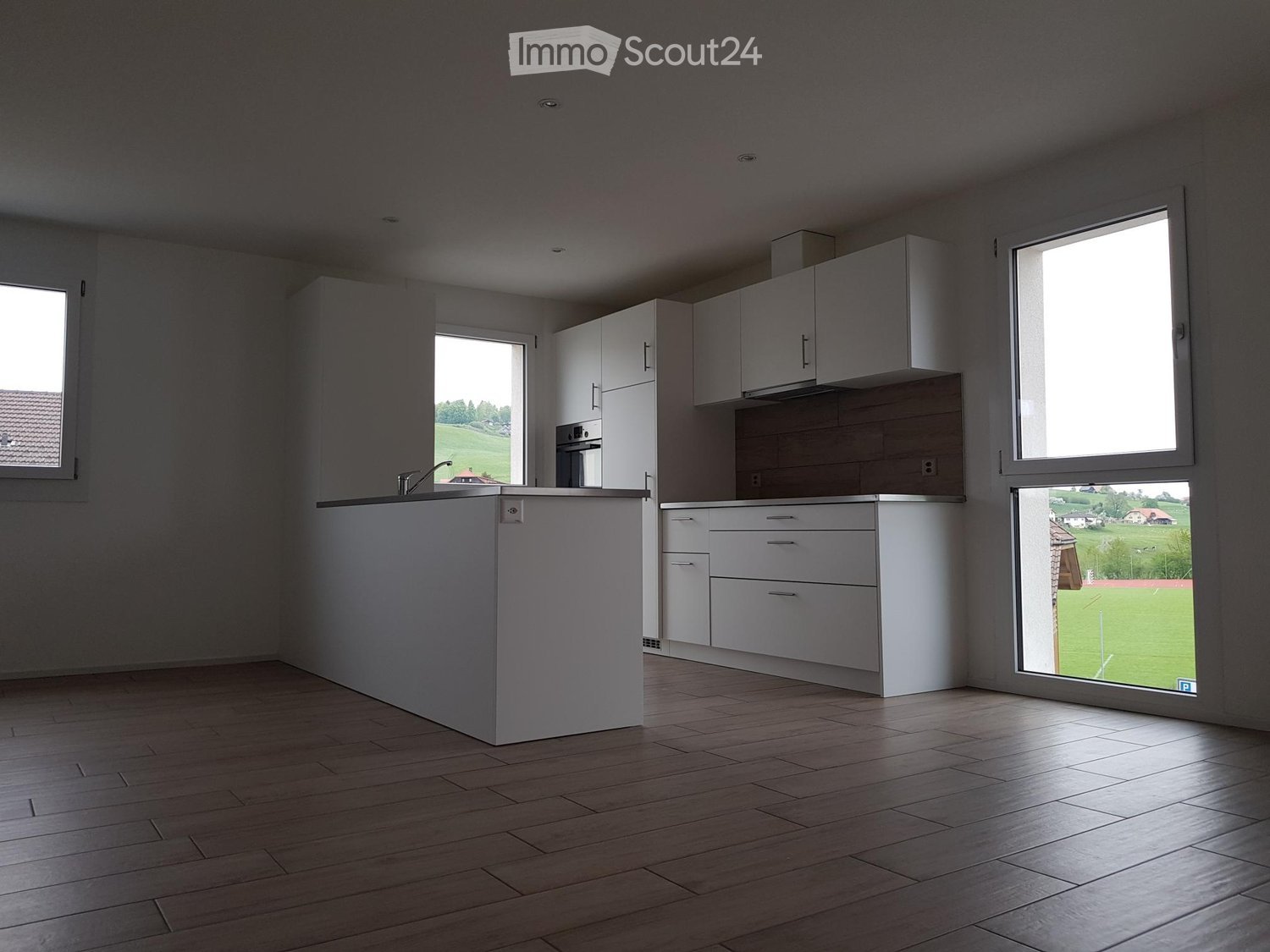 Open kitchen, white cabinets, wooden flooring, large windows, view of green field