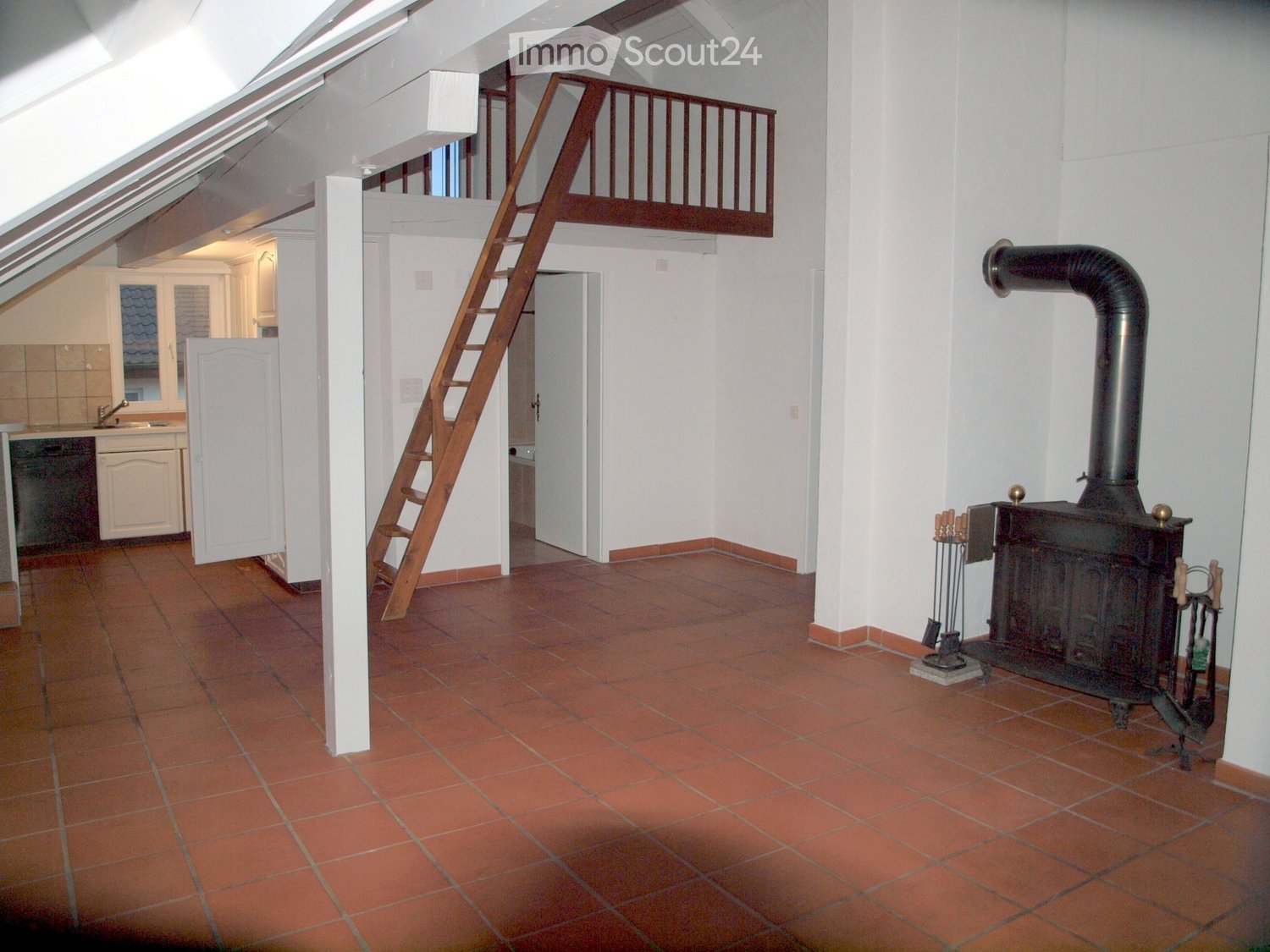 An attic room with red tile flooring, wooden ladder leading to an upper loft, white walls, a white cabinet, and a fireplace with chimney.