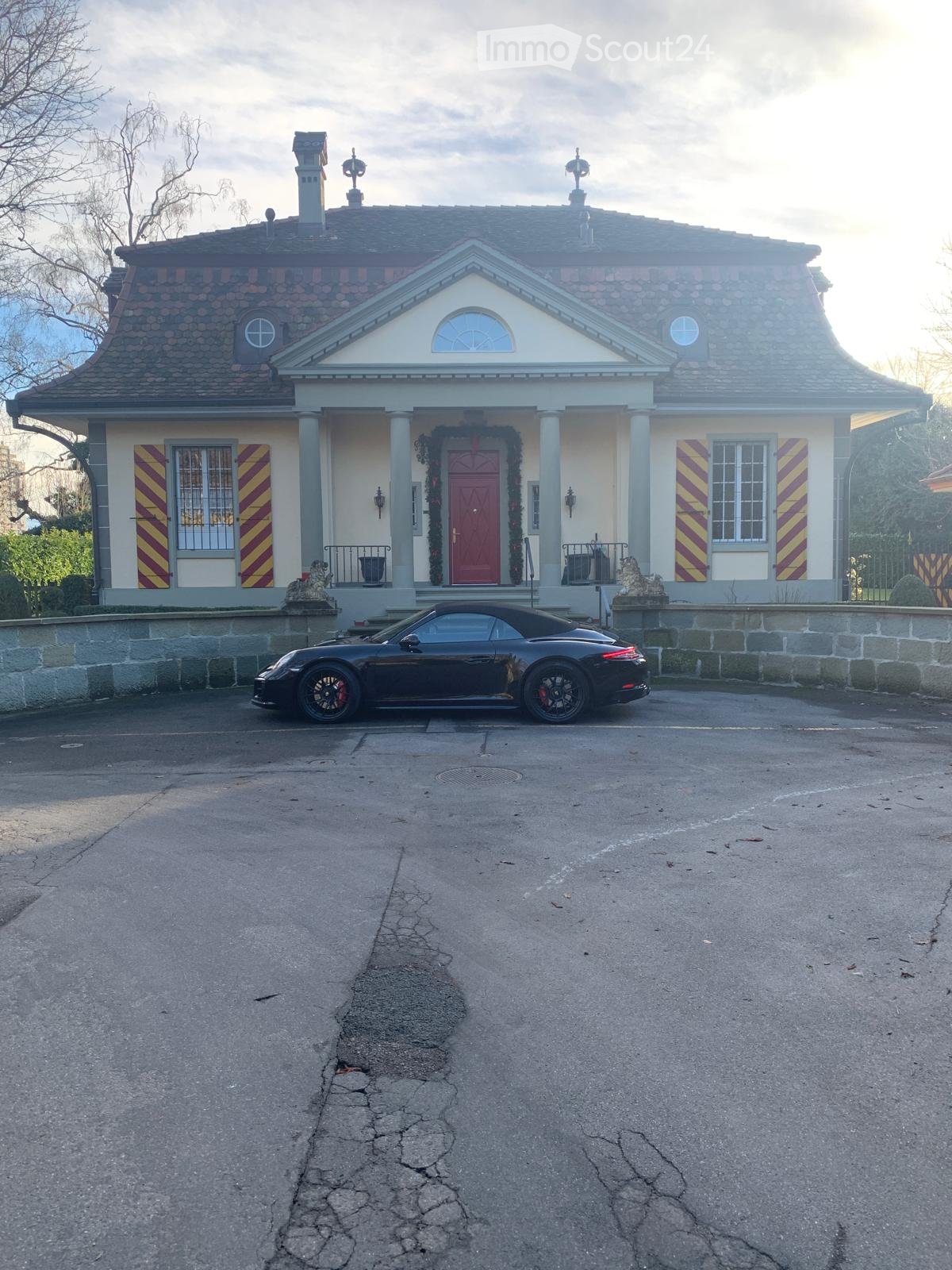 2-story house, red brick, white windows, stone wall, red door, 2 statues, parked black car