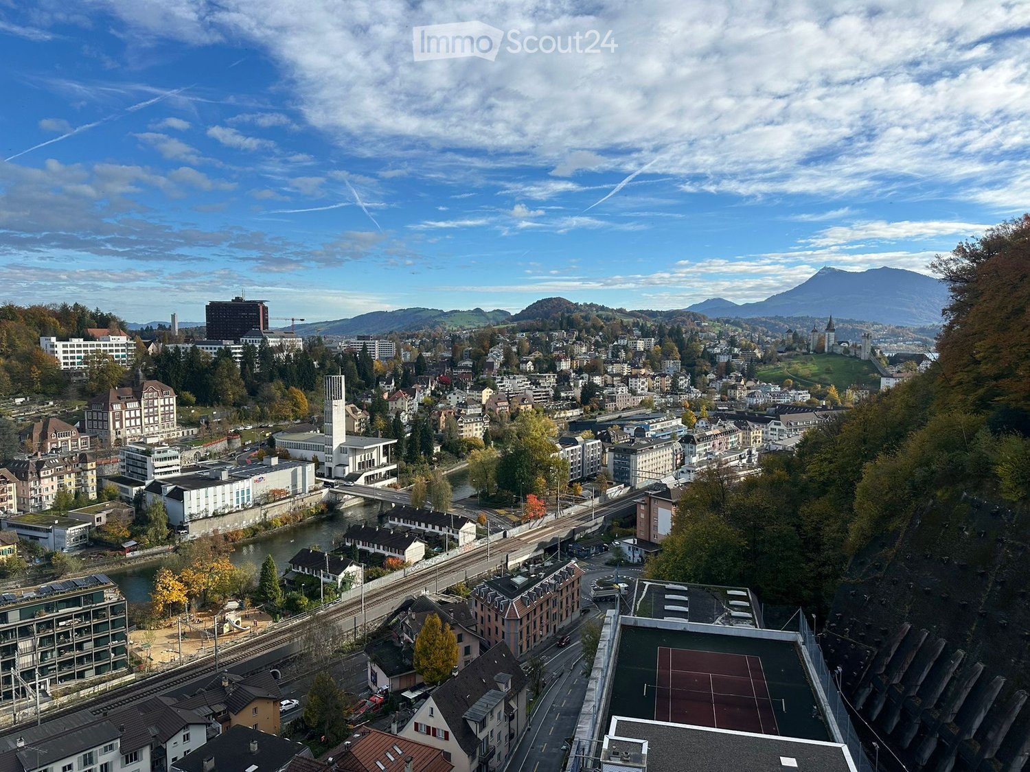 Aerial view of a town, various buildings, road, mountains, a river, and a sky with clouds