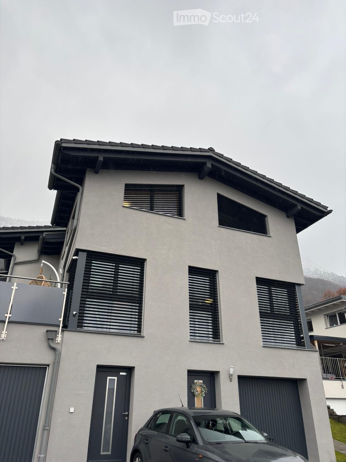 modern 2-story house, grey walls, black shutters, black garage doors, balcony