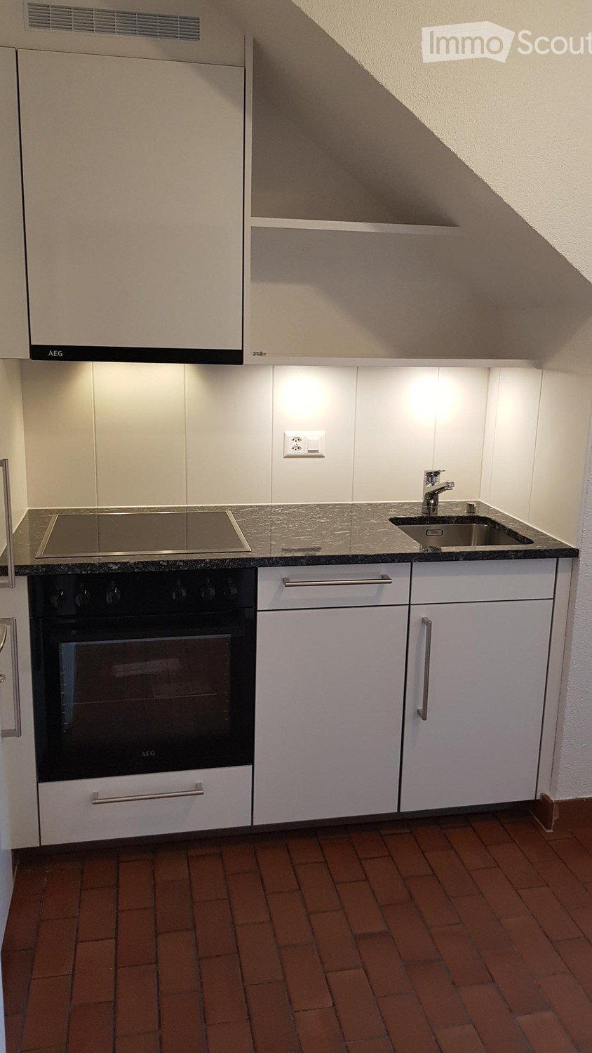 white cabinetry, black countertop, AEG oven and stove, stainless steel sink, wall socket, AEG brand logo