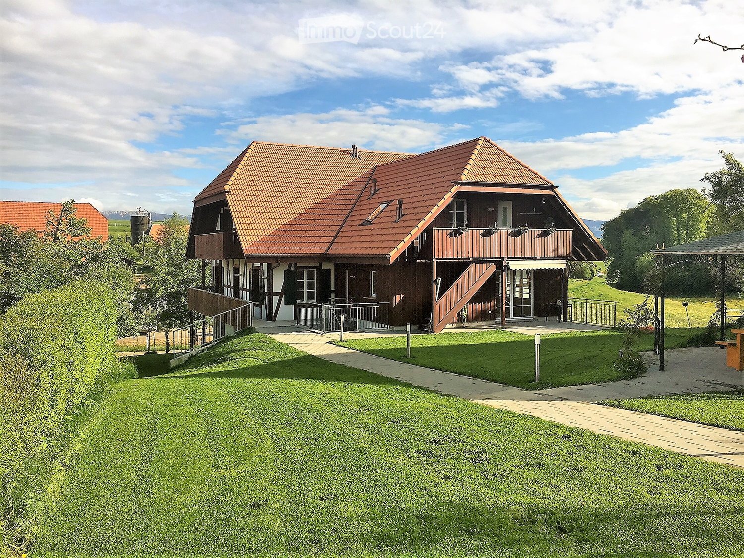 Wooden house, brown roof, raised ground floor, metal railings, large front yard, staircase