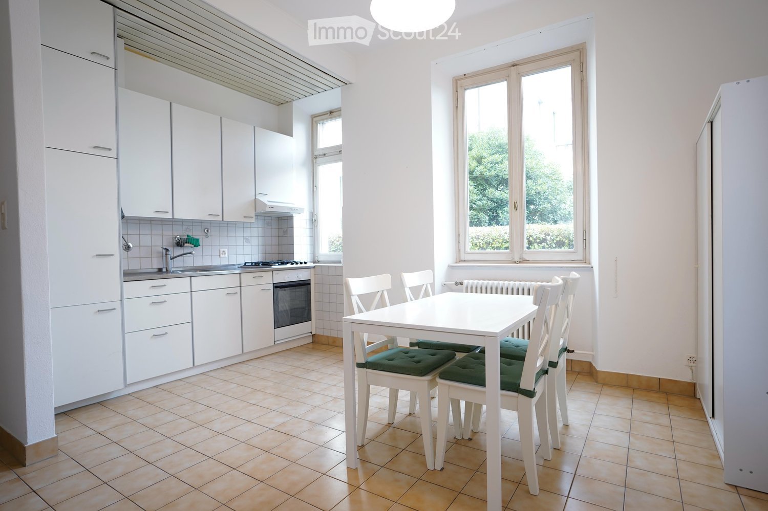 Kitchen with a dining area, white kitchen cabinets, stove, sink, windows, dining table, and chairs.