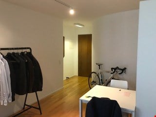 wooden floor, white walls, rack with jackets, table, chair, bicycle