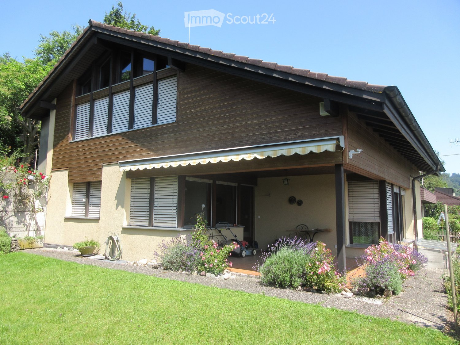 two story wooden house, raised ground floor, brown roof, awning, wooden terrace