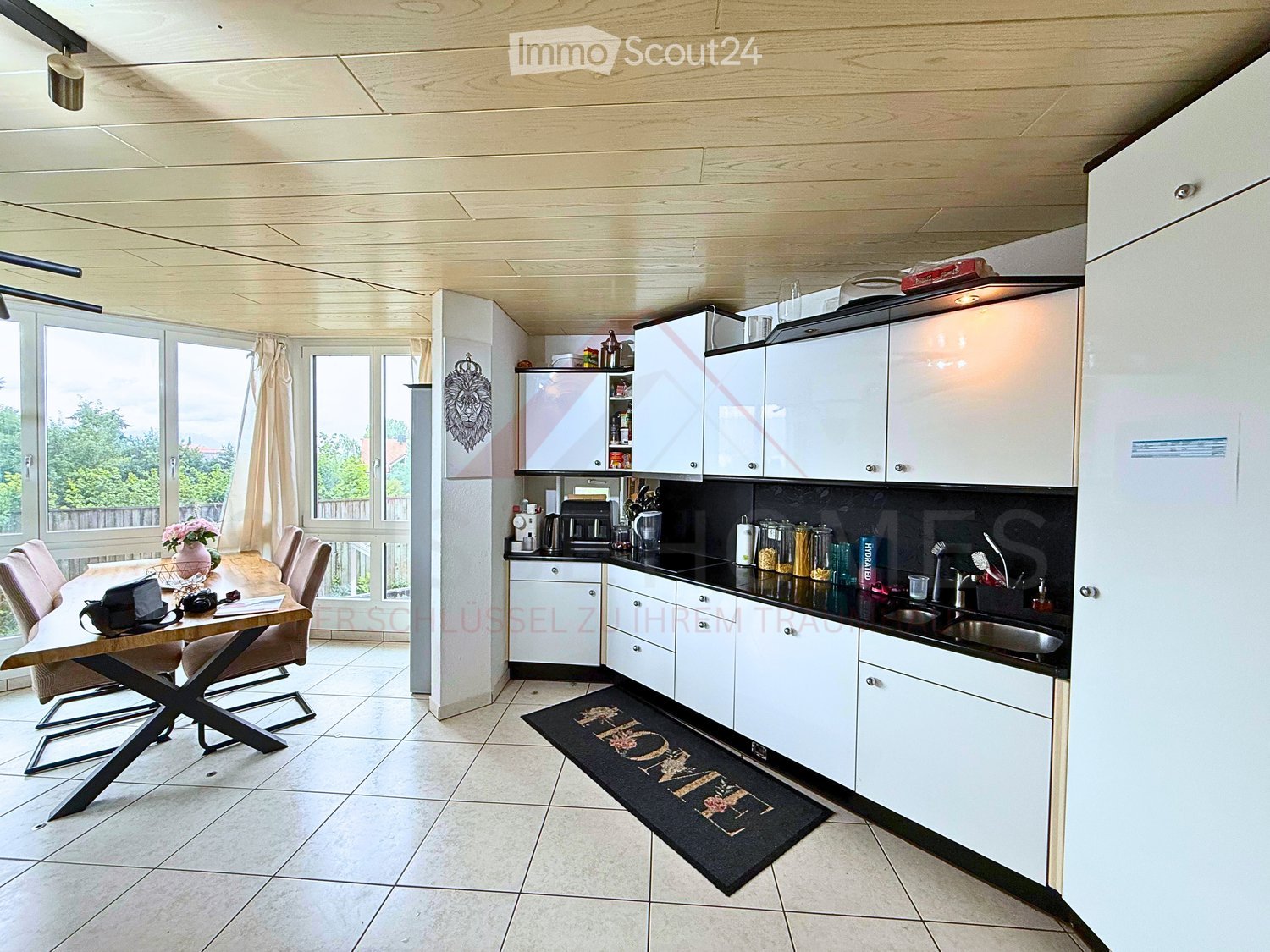 open plan kitchen with dining area, white cabinets, black countertops, two sinks, home mat, dining table with wooden top, black metal legs, chairs with cushions