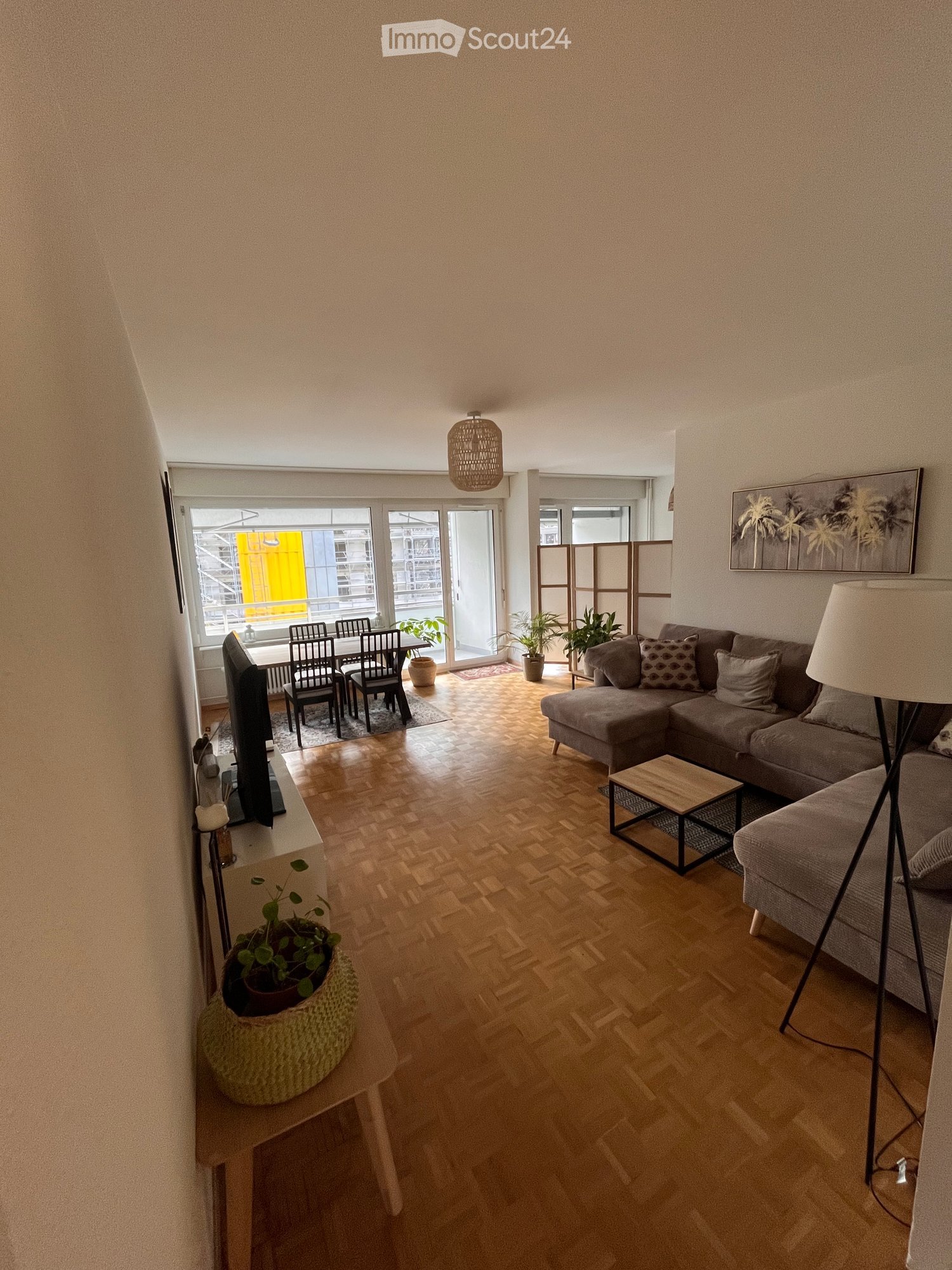 Large living room, couch, coffee table, table, chairs, TV, potted plants, wooden flooring, windows, lamps