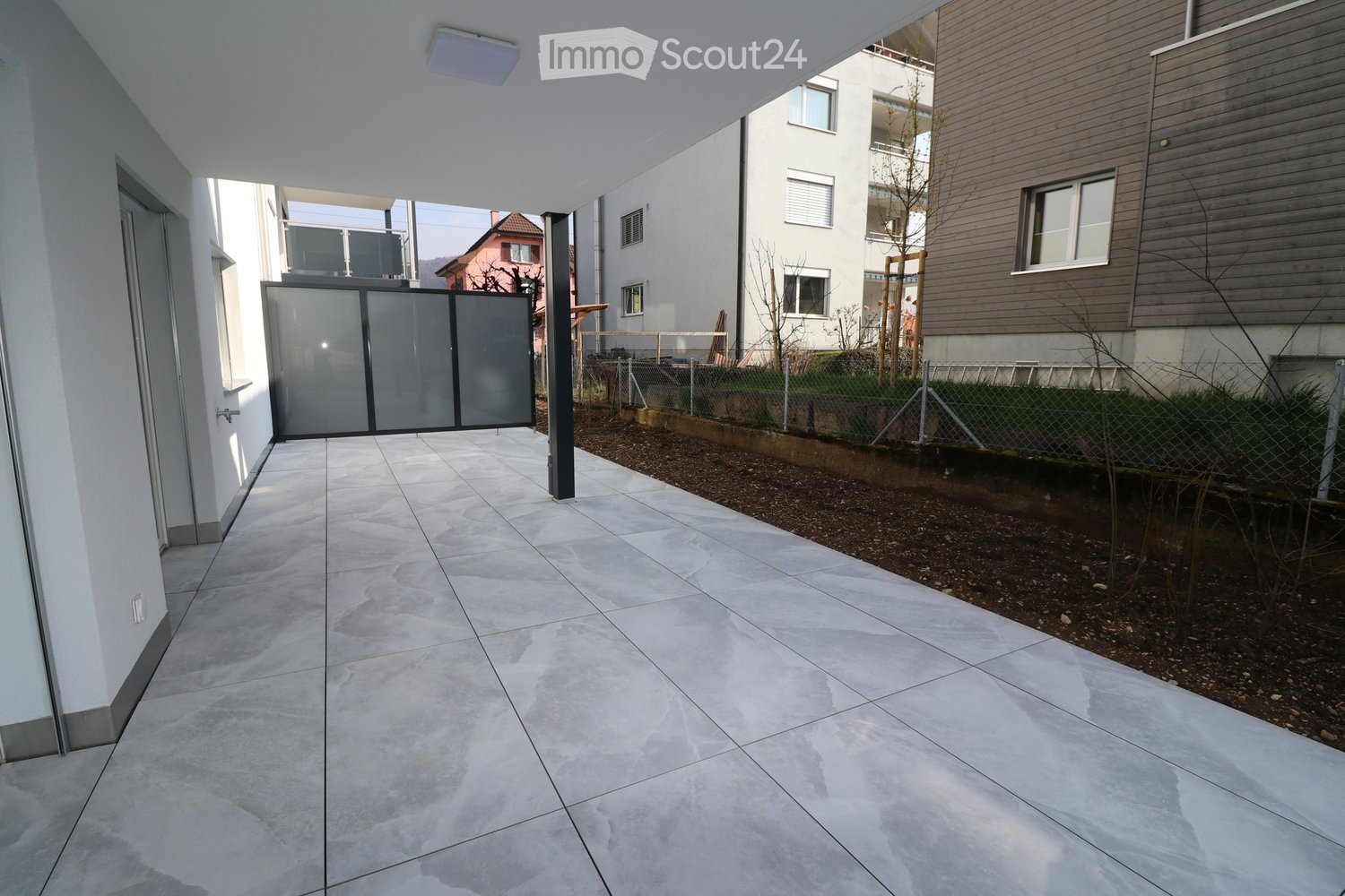 Terrace with grey tiles, grey wall with sliding glass door, black poles