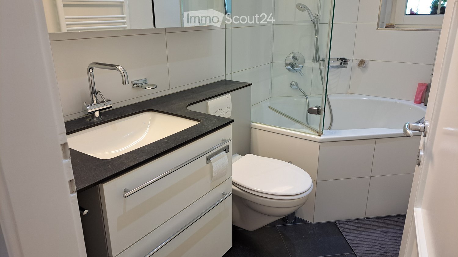modern bathroom with glass-enclosed bathtub, sink with faucet, toilet, and white tiles