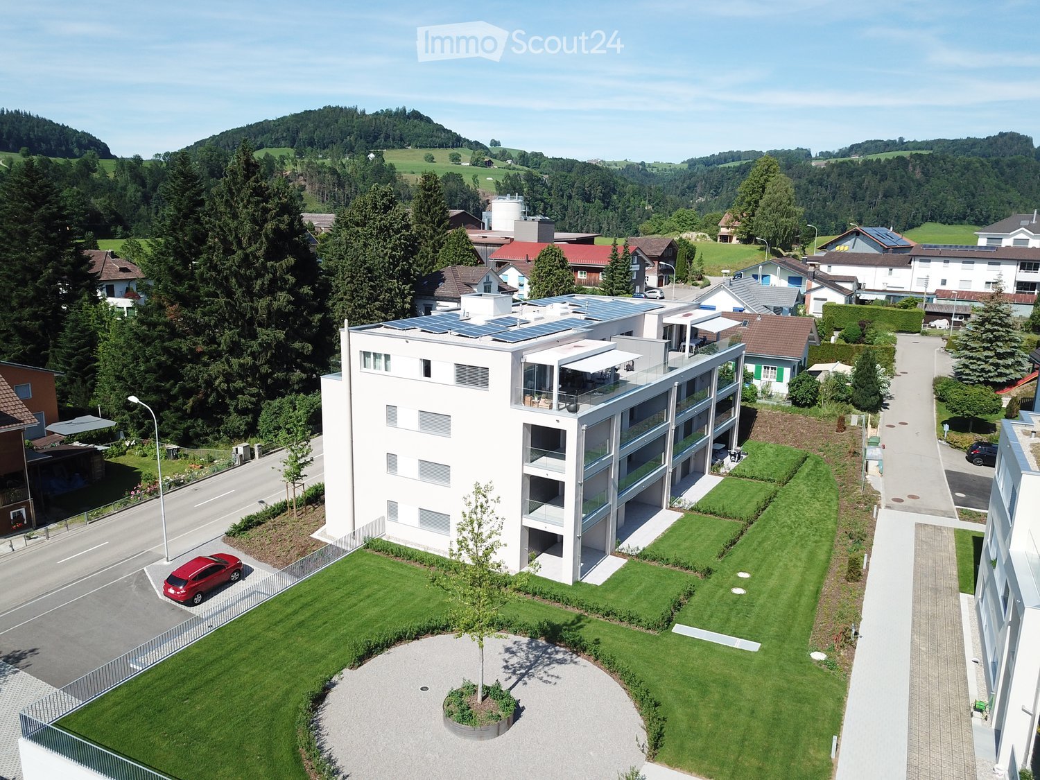 Apartment building with modern design, solar panels, rooftop terrace, grass, parking area