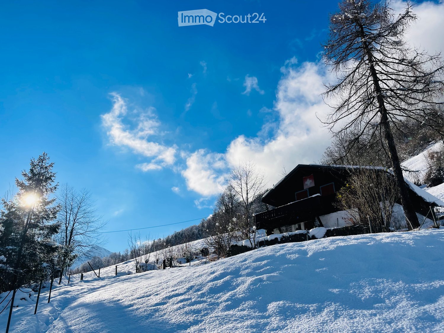 House with wooden balcony, situated on snowy mountain, surrounded by trees and fence