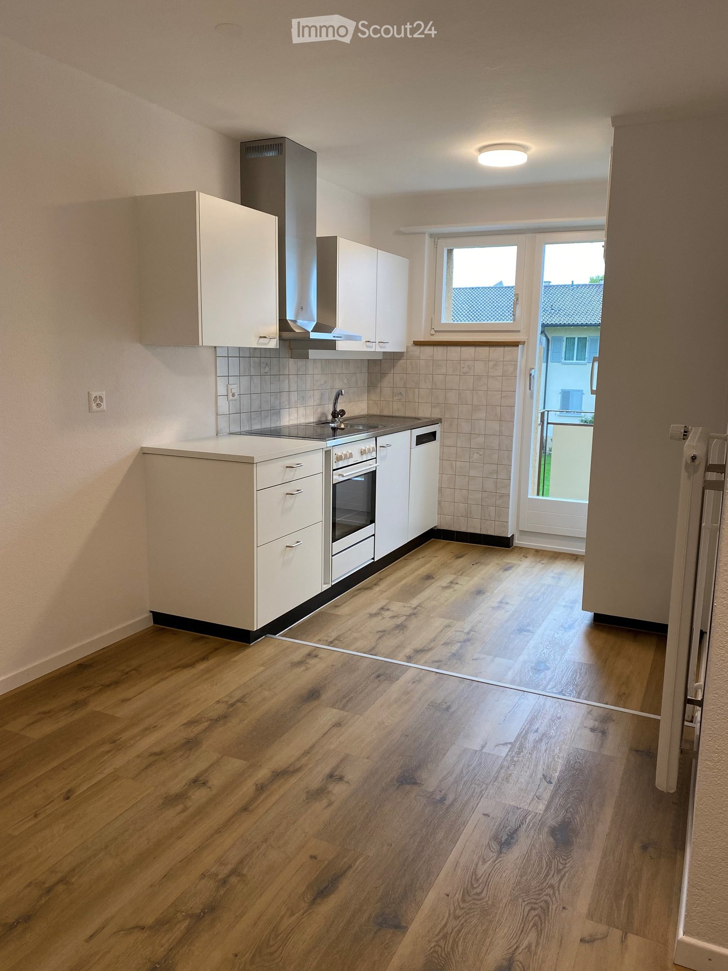 modern white kitchen, wooden floors, white tiles on walls, oven, sink, dishwasher, window to balcony