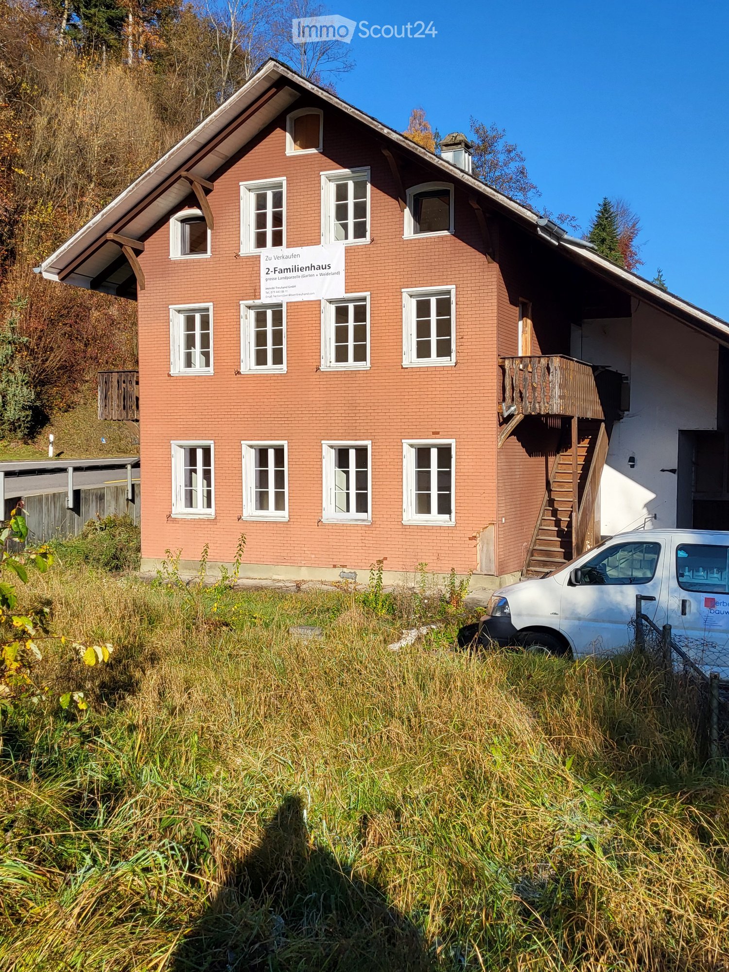 2 story brick house, multiple windows, wooden balcony with stairs, parked white van