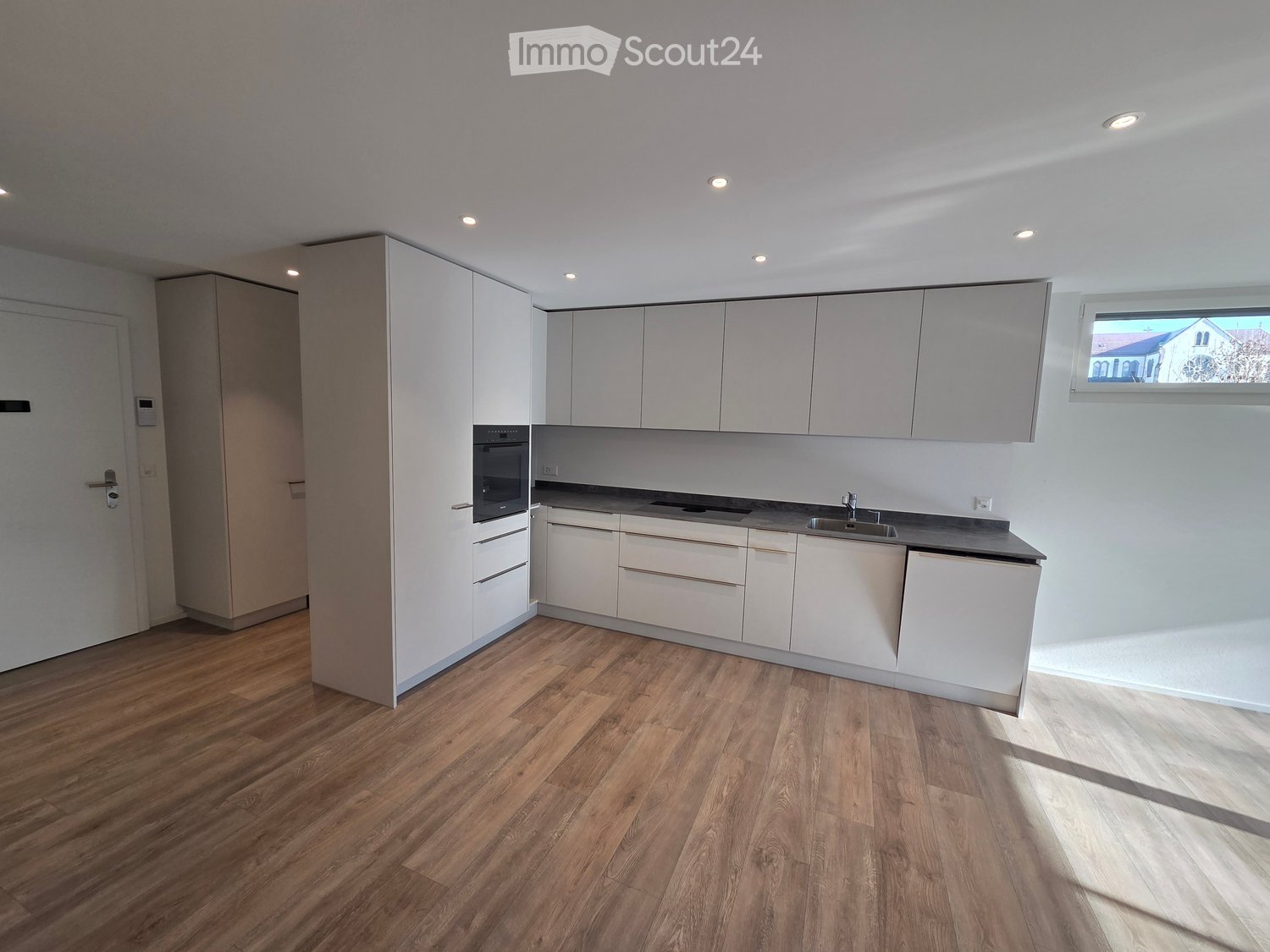 empty kitchen with white cupboards, wooden floor, integrated oven, sink