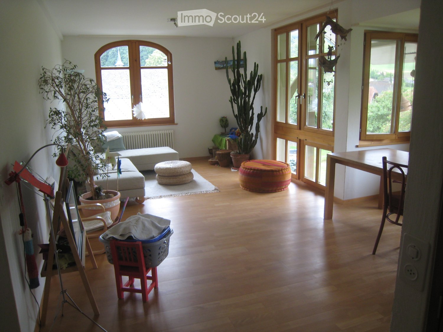 living room, large windows, radiator, couch, rug, wooden floors, plants, ottoman, table, chair, white painted wall