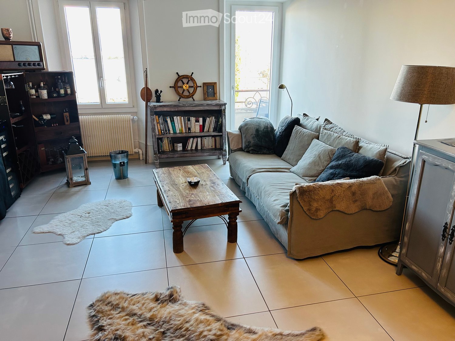wood floor, sectional couch, coffee table, white tiles, books, radiator, windows