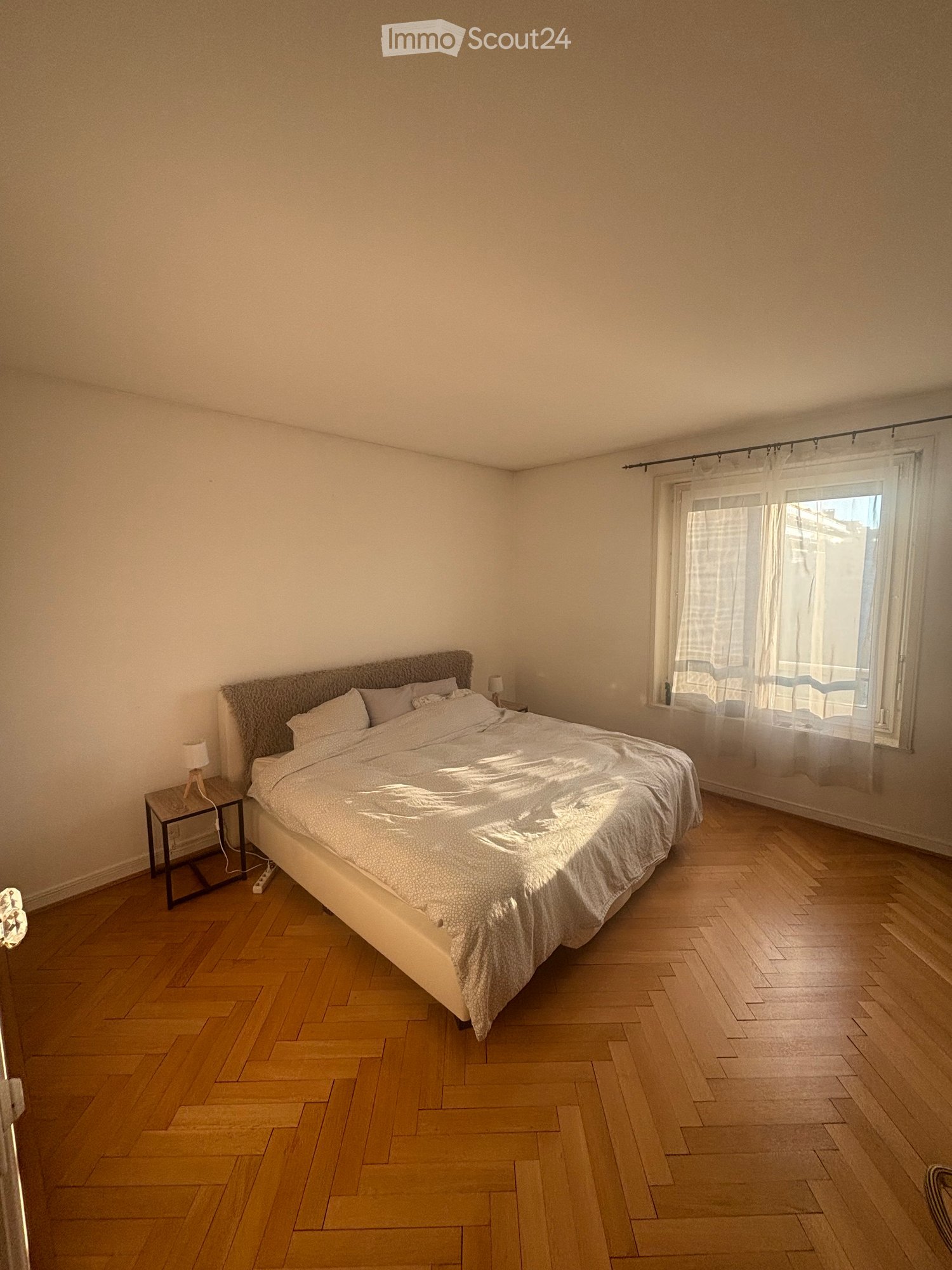 large bed, nightstands with lamps, parquet flooring, window with curtains
