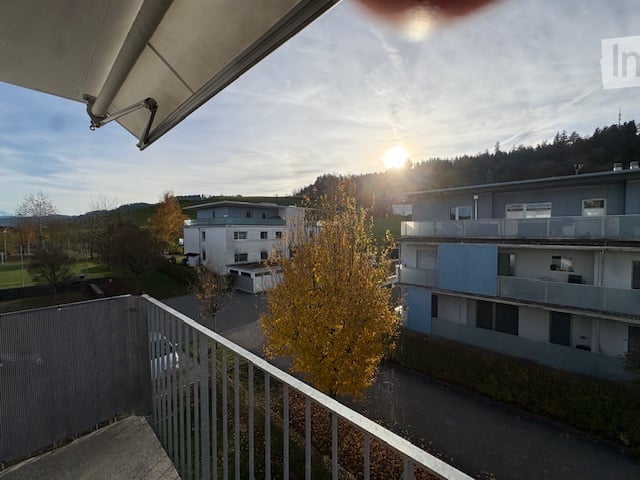 Balcony with fence, view of a neighborhood, a car in the driveway, a tree, and a bright sun
